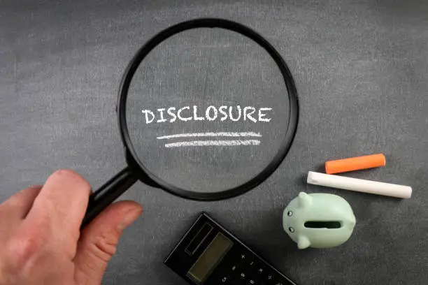 Photo of DISCLOSURE. Piggy bank, chalk pieces and magnifying glass on a blackboard