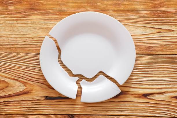 istock Top view on broken circle white plate on wooden background. The plate broke into three pieces. 1392138037
