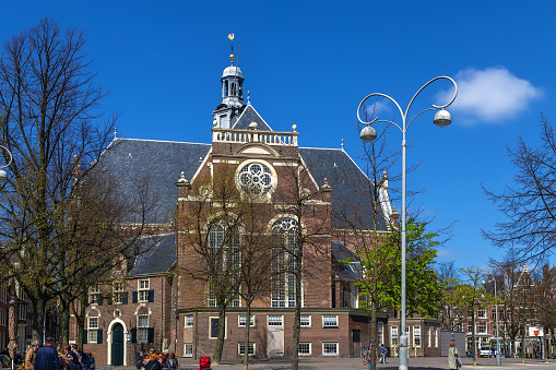 Oude Kerk Old Church in the Amsterdam Red Light disitrict with only a few  people on the square with blue sky in the background.