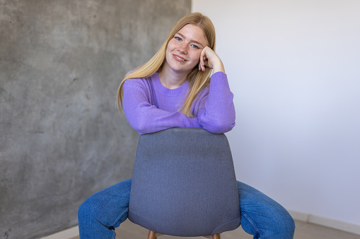 Portrait of young Caucasian woman sitting on the chair while wearing purple sweater