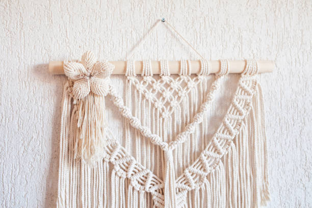istock Handmade macrame wall decoration with wooden stick hanging on a white wall. Macrame braiding and cotton threads. Female hobby. ECO friendly modern knitting natural decoration in interior 1392141074