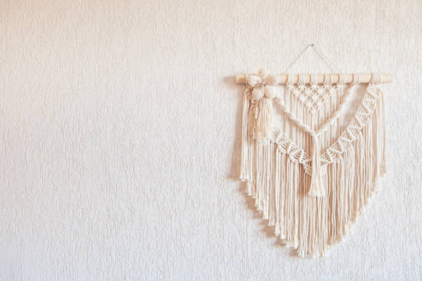 istock Handmade macrame wall decoration with wooden stick hanging on a white wall. Macrame braiding and cotton threads. Female hobby. ECO friendly modern knitting natural decoration in interior. Copy space 1392141075