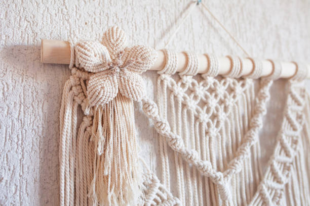 istock Handmade macrame wall decoration with wooden stick hanging on a white wall. Macrame braiding and cotton threads. Female hobby. ECO friendly modern knitting natural decoration in interior 1392141077