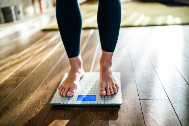 Female is checking her weight on the scale Low section of woman checking her weight on the scale at home scales stock pictures, royalty-free photos & images