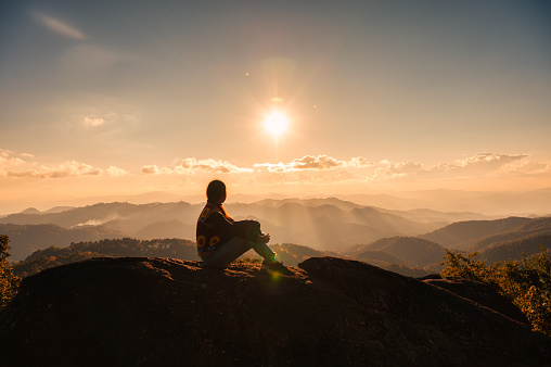 Successful silhouette young hiker woman relaxing and enjoying the sunset view on top of mountain peak at national park