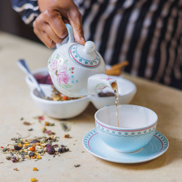 istock Tea making. African-American woman makes traditional herbal tea using a classic teapot, pouring the tea into a cup. Close-up photo with hands only. 1392144096
