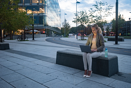 Young businesswoman looking at laptop while sitting on the bench in city