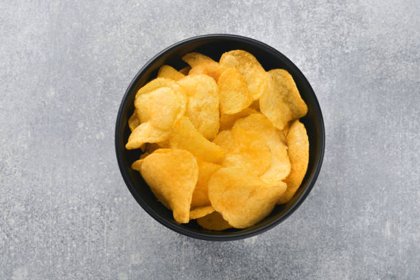 Potato chips. Fast food. Crispy potato chips ceramic black bowl with sour cream sauce and onions in wooden stand on gray kitchen table concrete background. American tradition. Hot BBQ. Top view. patatas fritas. comida rápida. crujiente patata fritas tazón negro de cerámica con salsa de crema agria y cebollas en soporte de madera sobre fondo de hormigón gris de la mesa de cocina. tradición americana. barbacoa caliente. vista superior.