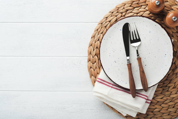 istock Vintage zero waste silverware. Rustic vintage set of white plate, wooden spoon and fork on napkin for dishes from water hyacinth on light gray concrete background. Empty dishes. Top view. Mock up. 1392148191