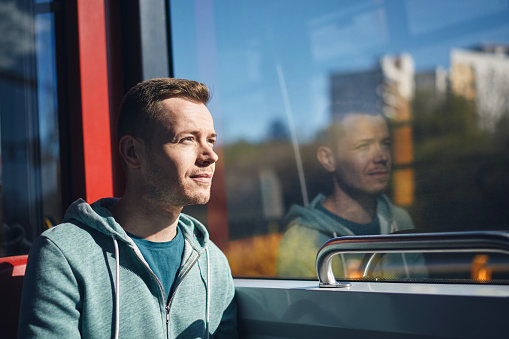 Man commuting by tram. Adult passenger looking out window of train of public transportation. 