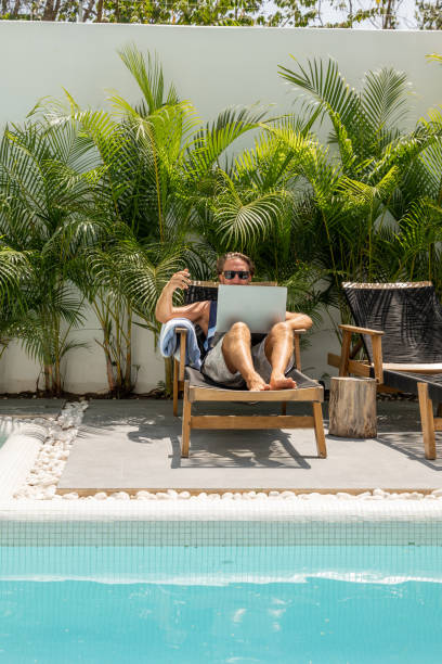 istock Young man working online by the pool, he uses a laptop 1392149854