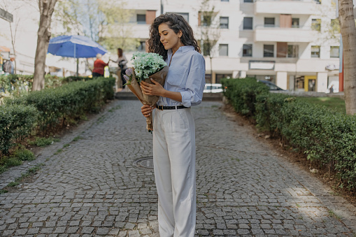 Young beautiful woman walks around city with bouquet of flowers and  enjoys  on spring day