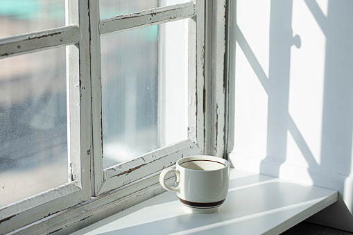A cup of coffee on the white floor in the sunshine beside window