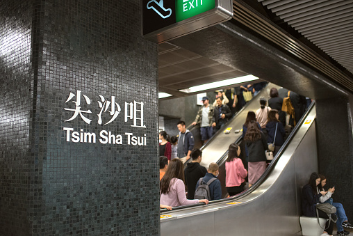 Kowloon, Hong Kong - December 7, 2018: Name sign of Tsim Sha Tsui Subway Station and passengers on escalator.