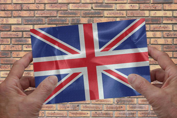istock Hands holding a small UK fabric flag   Brick wall background 1392152250