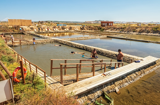 Castro Marim, Portugal - July 30, 2021: People applying saline clay to their bodies and floating in the mineral waters of the salt pans.
In a part of the Castro Marim salt pans, people can take advantage of the mineral properties of salt for their well-being and health, covering the body with saline clay and by floating in the waters of the salt pans.