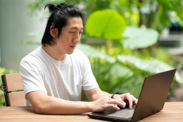 istock Young Asian Man working on Laptop in Garden Background 1392154031