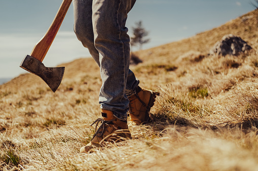 Bottom part of body, man wearing jeans, holding an ax, standing on the hill.