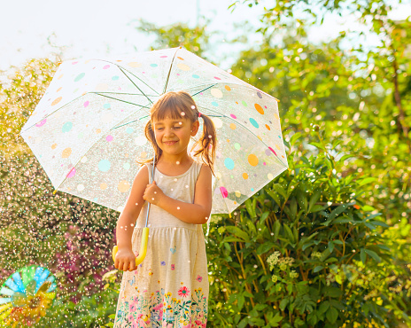 Happy little girl with an umbrella under the summer rain.