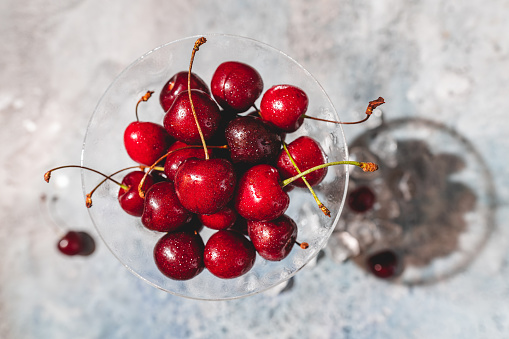 Top view of a ripe sweet cherry in a glass on light blue background