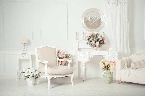 Beautiful luxury classic white bright clean interior bedroom in baroque style with large window, armchair and flower composition