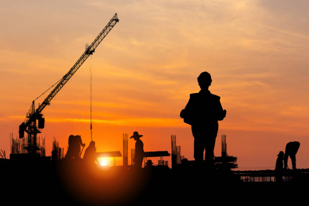 istock Silhouette of Engineer with blueprint and foreman worker team at construction site with blurred sunset sky background 1392161955