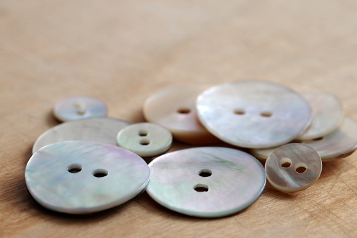 Buttons made of natural mother of pearl on a background of wooden texture. Selective focus.