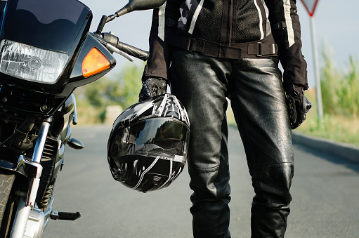 A woman biker holds a protective helmet in her hand, standing next to a motorcycle. Close-up.