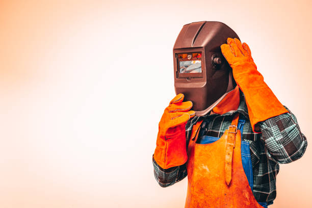 Heavy industry worker in a protective suit with a mask to protect the eyes and face, fiery colors, Space for text Heavy industry worker in a protective suit with a mask to protect the eyes and face, fiery colors, Space for text welding mask stock pictures, royalty-free photos & images