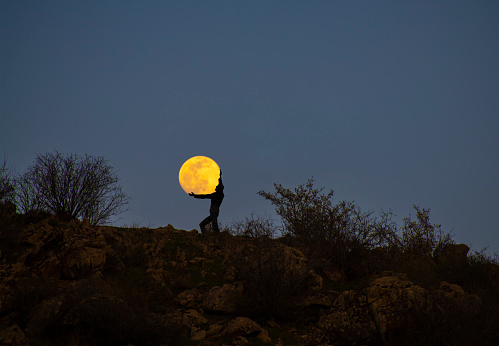 Silhouette of a person stands on the hill and keep in the arms full moon