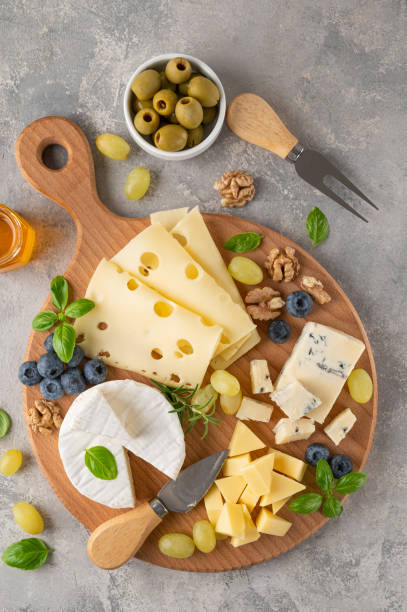 piatto di formaggi con una varietà di formaggi, miele, uva, noci, olive, mirtilli ed erbe fresche su uno sfondo concreto. uno spuntino festivo. vista dall'alto, spazio di copia. - fruit and cheese foto e immagini stock