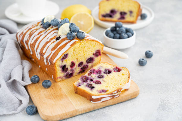 istock Lemon blueberry cake with lemon icing and fresh berries on top on the board on a gray concrete background with cup of tea. Selective focus. Copy space. 1392170328