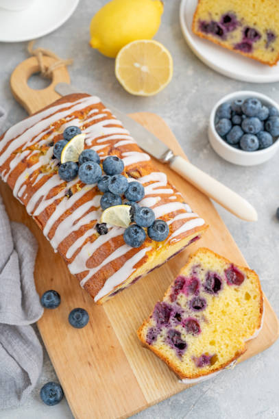 istock Lemon blueberry cake with lemon icing and fresh berries on top on the board on a gray concrete background with cup of tea. Selective focus. Copy space. 1392170339