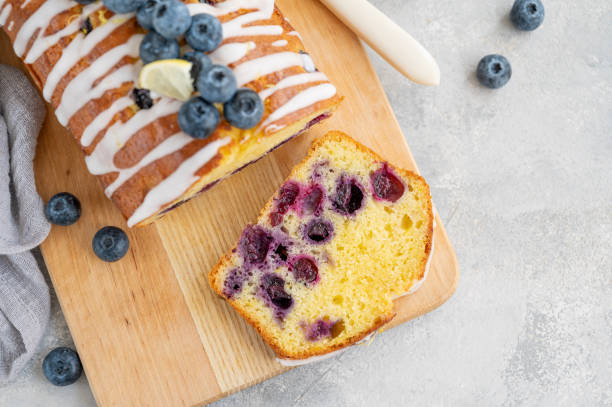 istock Lemon blueberry cake with lemon icing and fresh berries on top on the board on a gray concrete background with cup of tea. Selective focus. Copy space. 1392170348