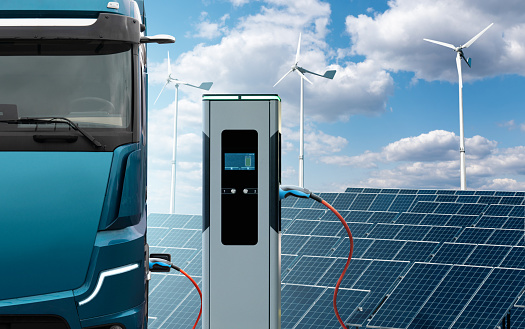 Electric truck with charging station on a background of solar panels and wind turbines. Concept