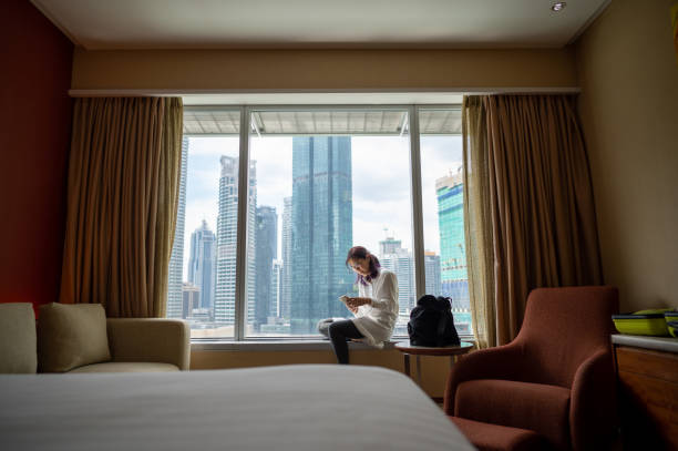 retrato de uma turista asiática usando smartphone em quarto de hotel após check-in - conceito de viagem solo - urban scene business travel travel asia - fotografias e filmes do acervo