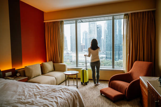 Portrait of An Asian tourist woman standing nearly window, looking to beautiful view with her luggage in hotel bedroom after check-in stock photo