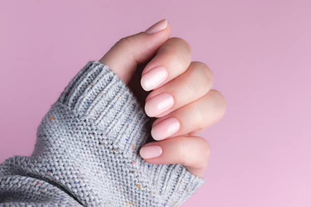 Hand in sweater with nude nails on pink background Female hand in gray knitted sweater with natural beautiful manicure - pink nude nails on pink background. Nail care concept nude coloured stock pictures, royalty-free photos & images