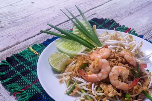 Pad Thai with fresh shrimp in a white plate on wooden table.