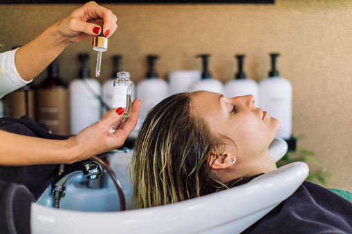 Beautiful young woman getting her hair washed in hair salon. She is relaxing with her eyes closed while the hairdresser massages her scalp and washes her hair with shampoo, hair treatment and water.