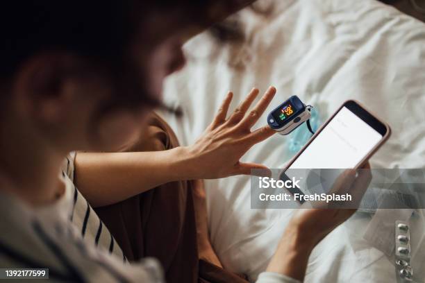 A From Above Shot Of An Unrecognizable Woman Measuring The Oxygen Saturation Level Of Her Blood After Recovering From Coronavirus While Watching Something On Her Smartphone Stock Photo - Download Image Now