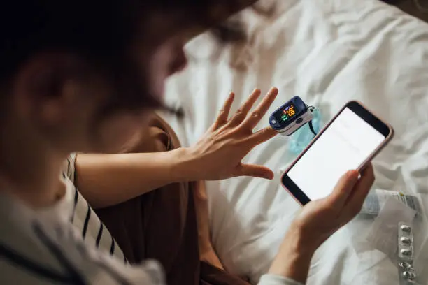 Photo of A From Above Shot Of An Unrecognizable Woman Measuring The Oxygen Saturation Level Of Her Blood After Recovering From Coronavirus While Watching Something On Her Smartphone