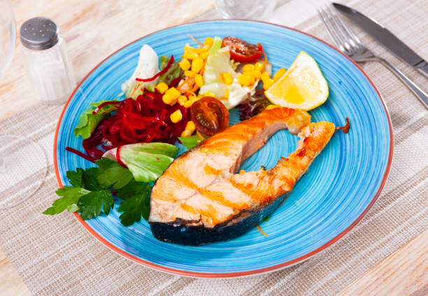 Grilled salmon steak with vegetable salad, made from corn, cherry tomatoes, lettuce leaves and grated beetroot, served with a slice of lemon