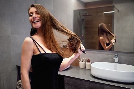 Portrait of young woman combing her hair in bathroom