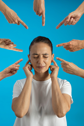 All fingers pointing at a woman. Woman over blue background covering ears with fingers.