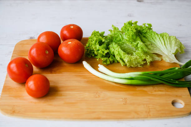 Fresh vegetables for salad lie on a wooden table with a cutting board. Close-up.