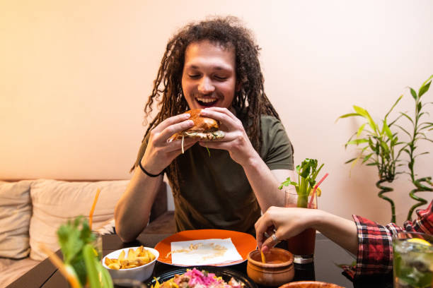 istock Young man with dreadlocks enjoying eating burger and drinking cocktail 1392190769