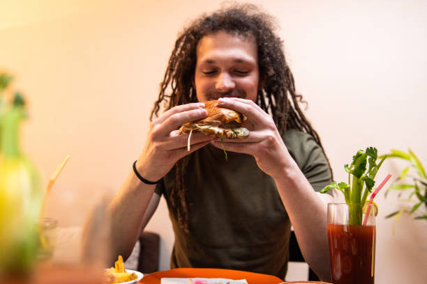 istock Young man with dreadlocks enjoying eating burger and drinking cocktail 1392190797