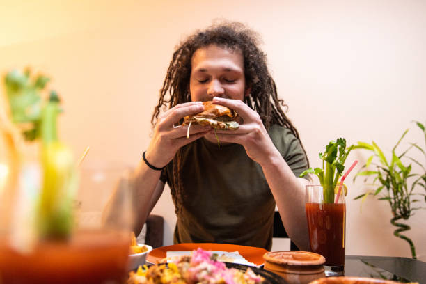 istock Young man with dreadlocks enjoying eating burger and drinking cocktail 1392191326