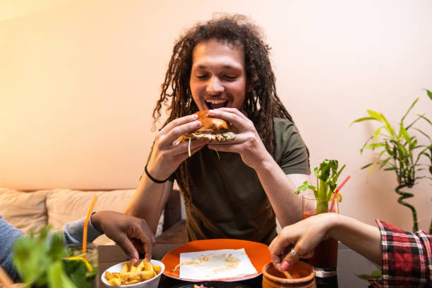 istock Young man with dreadlocks enjoying eating burger and drinking cocktail 1392191360